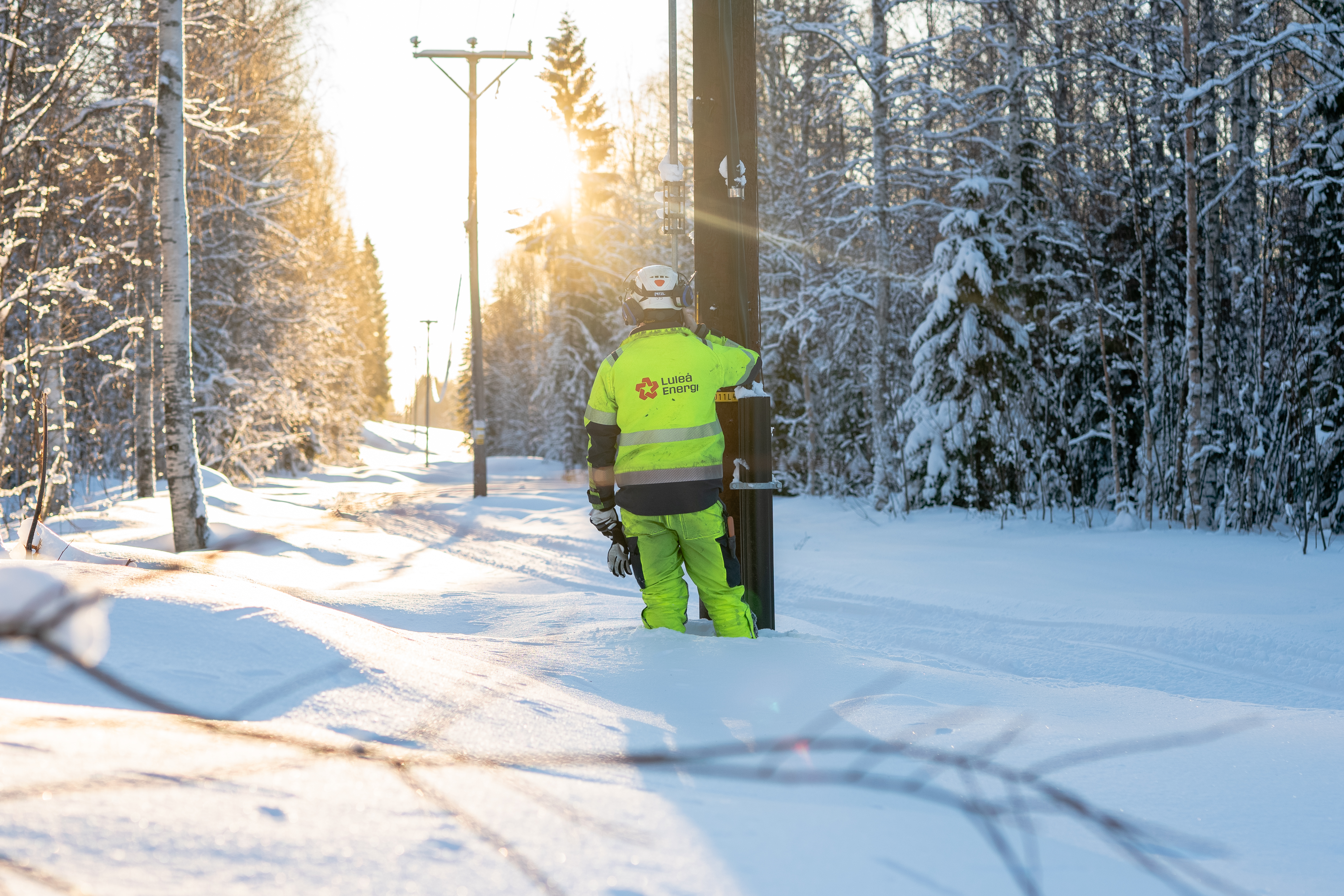 Person i varselkläder bredvid en elkraftstolpe. Vinter